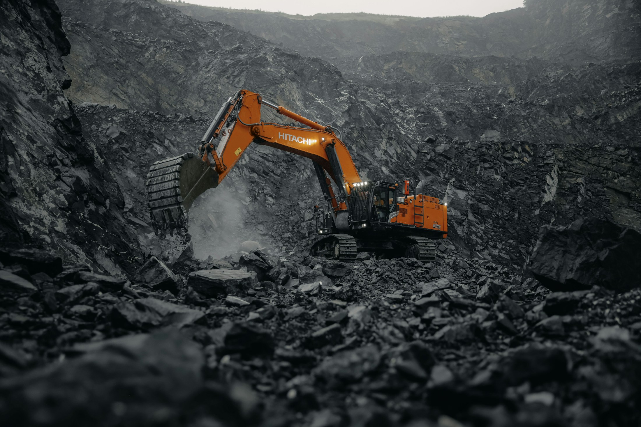 An excavator loading broken basalt into a haul truck at a quarry's working face.