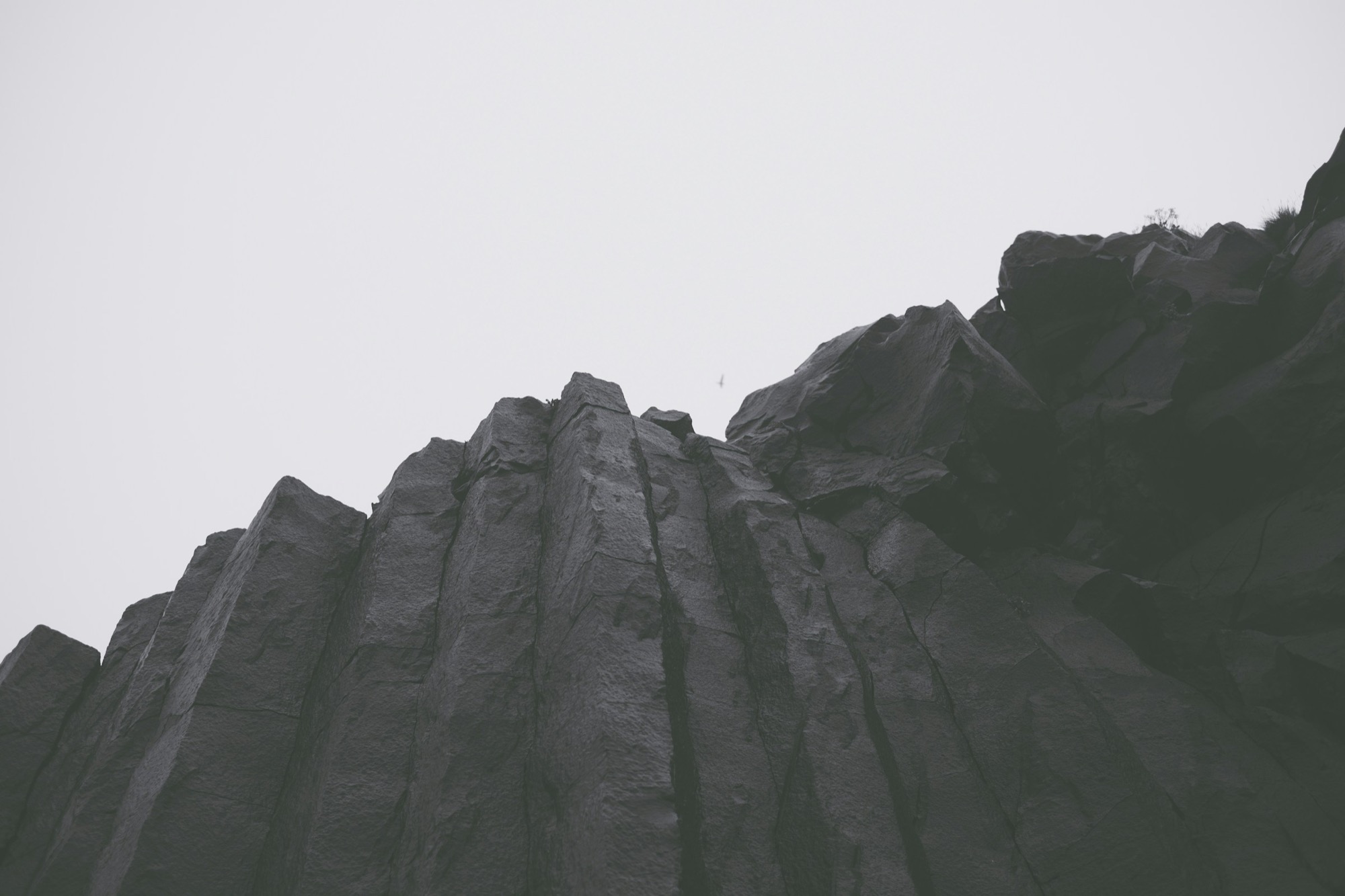 A dark basalt rock mass photographed from below against an overcast sky.