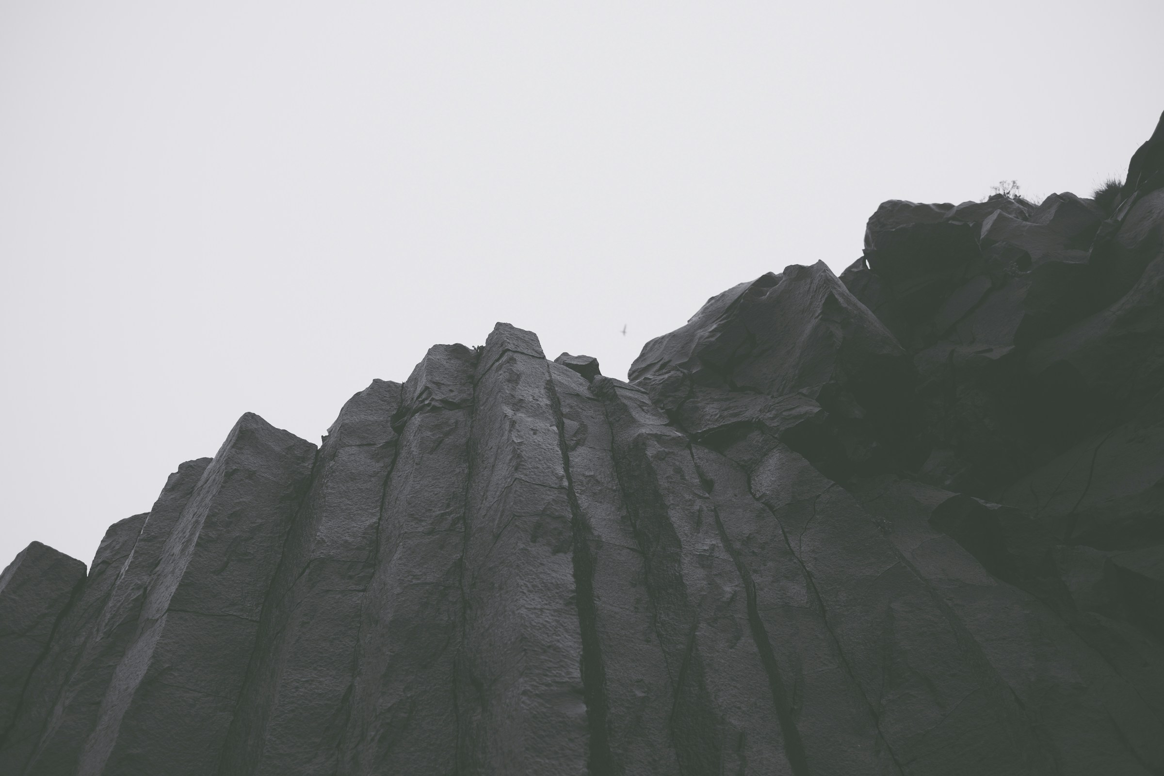 A dark basalt rock mass photographed from below against an overcast sky.