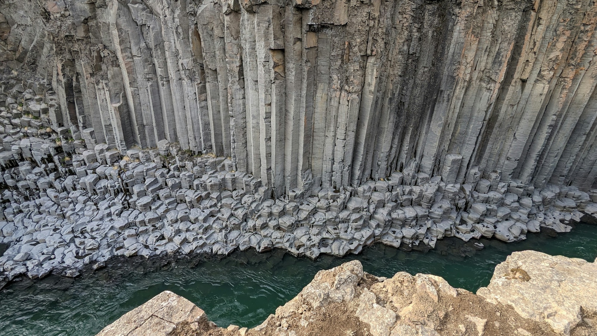 The base of a basalt colonnade meeting still water.